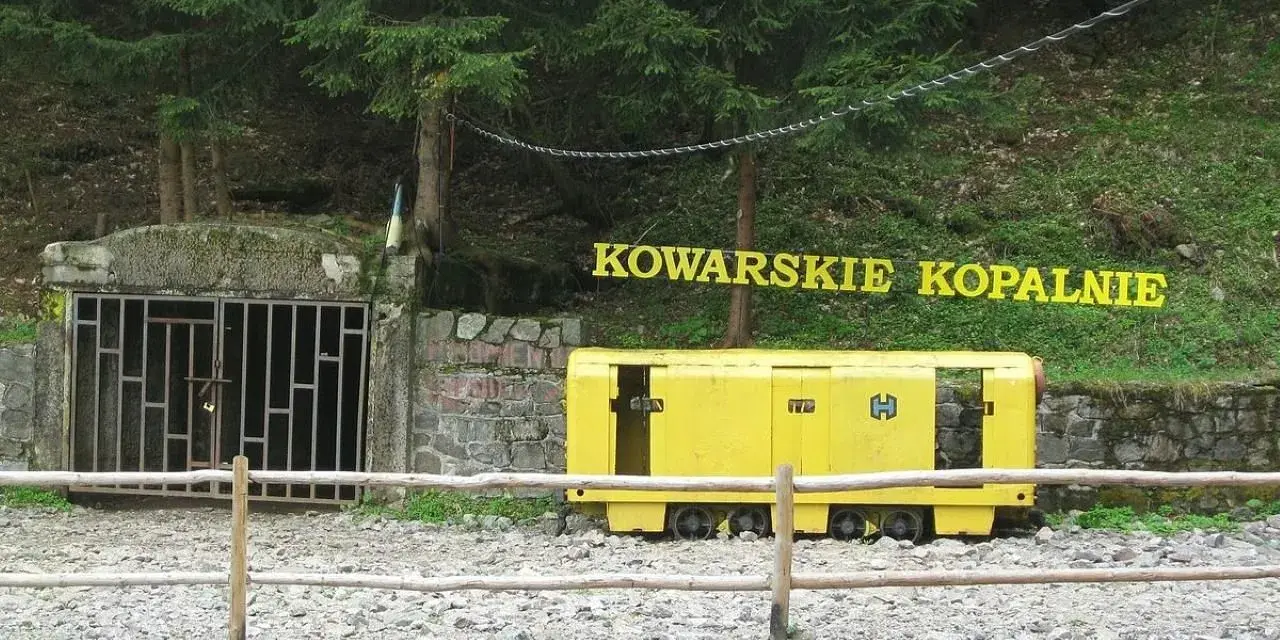 Wejście do sztolni Kowary z żółtym wagonikiem górniczym i napisem "KOWARSKIE KOPALNIE".