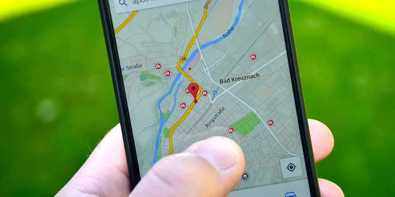 Palec wskazuje na mapę GPS w telefonie, szukając apteki w pobliżu. W samochodzie taka nawigacja to podstawa.
