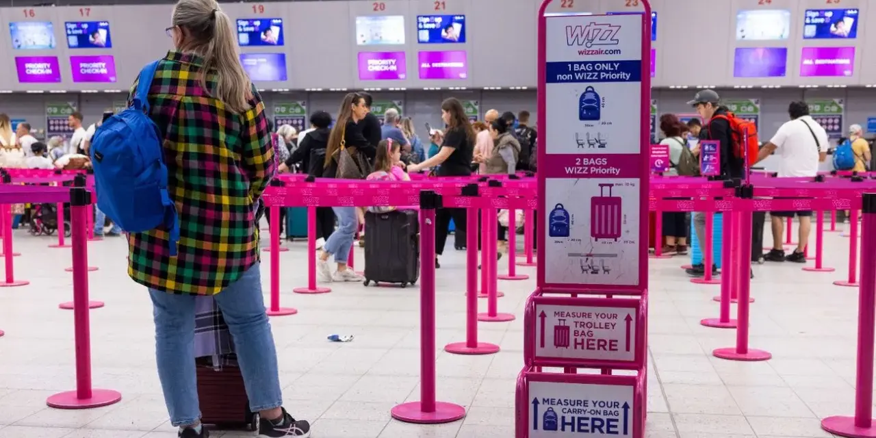 Kolejka do odprawy Wizzair. Tablica informuje, co trzeba wyjąć z bagażu podręcznego: płyny, elektronikę i przedmioty ostre.
