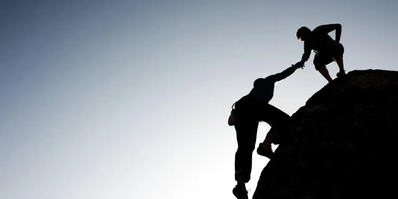 Silhouette d'un grimpeur aidant un autre à atteindre le sommet. Une belle présentation photographe de l'entraide et de la persévérance.