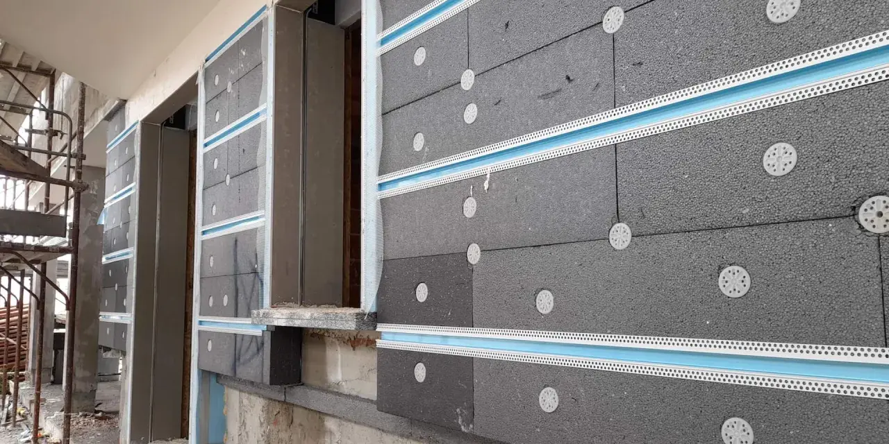 Pannelli grigi per cappotto termico ignifugo, fissati con tasselli bianchi e profili azzurri, in fase di installazione su un edificio.