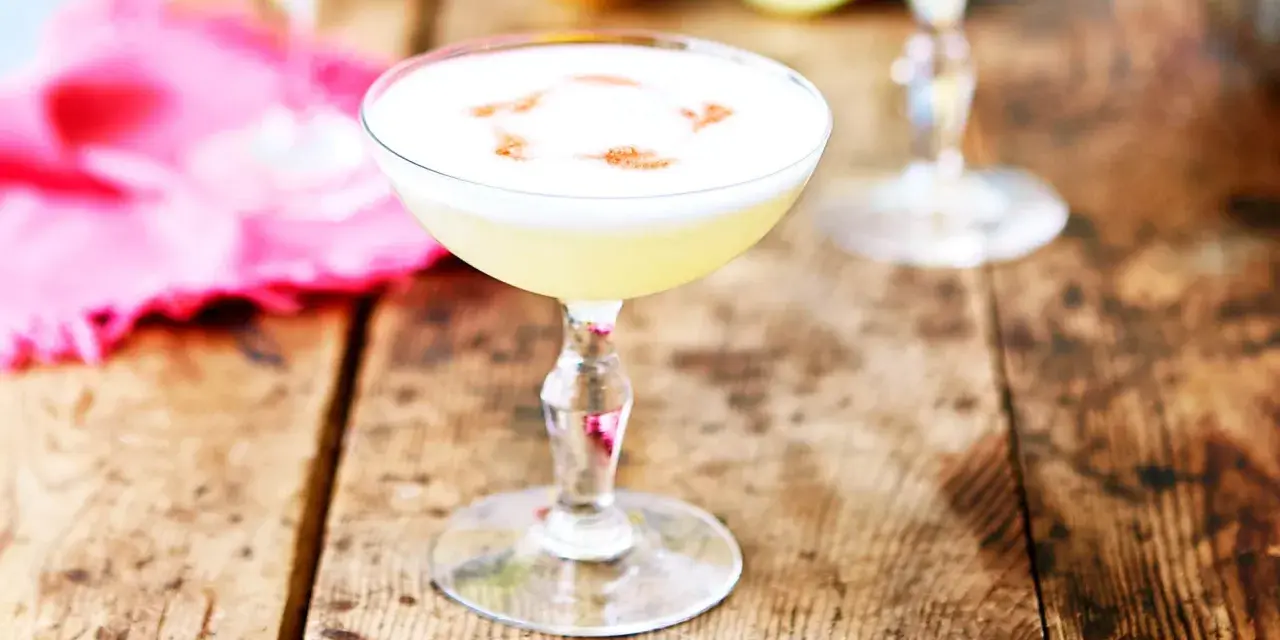 En krämig pisco sour med ett vitt skum och en touch av kanel på en rustik träyta.