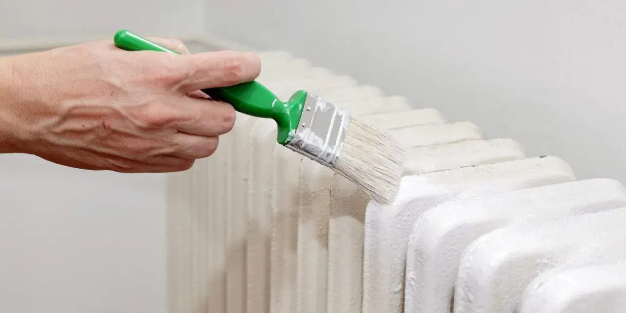 Main d'une personne peignant un radiateur en fonte avec une brosse.