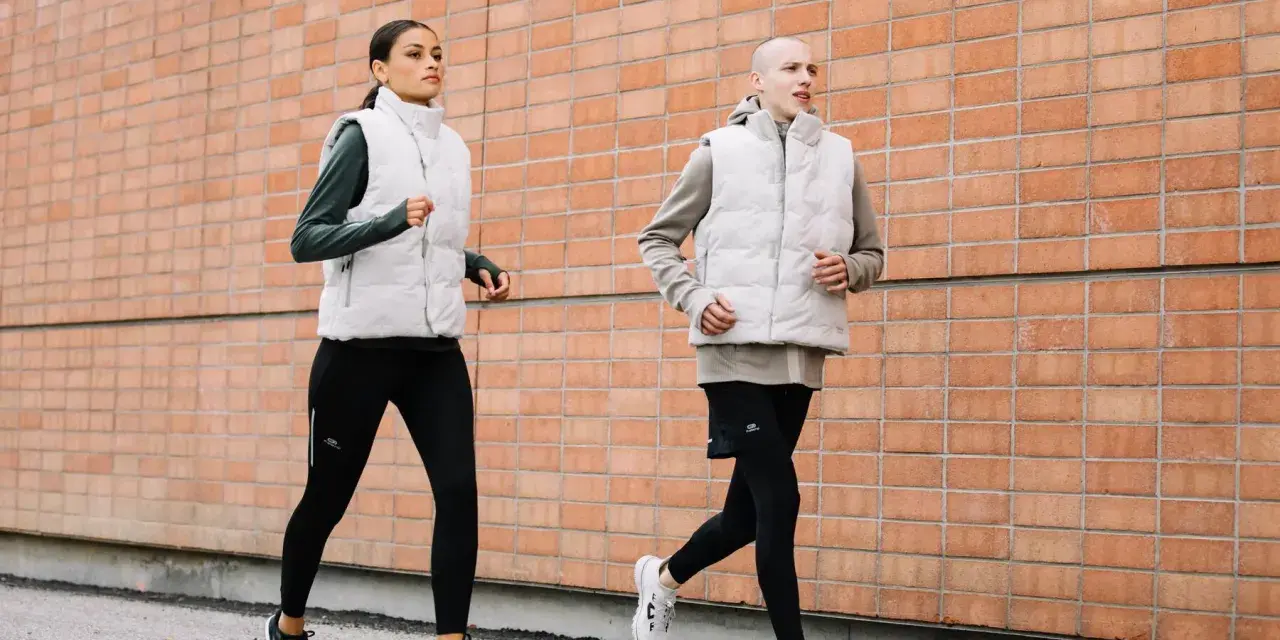 Coppia corre lungo un muro di mattoni. Ottimi consigli per correre in coppia, con abbigliamento tecnico.