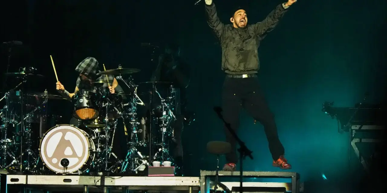 Linkin Park-Bandmitglieder auf der Bühne, ein Sänger springt, ein Schlagzeuger spielt.