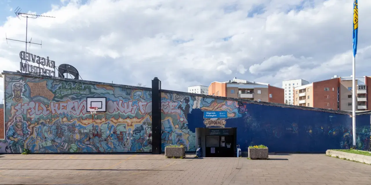 En stor vägg täckt av färgstark graffiti. En basketkorg hänger på väggen.