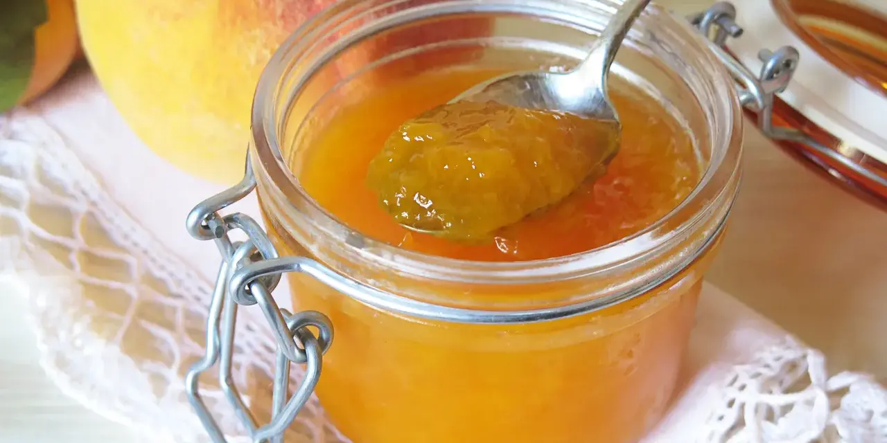 Cuchara con mermelada de melocotón casera, junto a melocotones frescos y un tarro de cristal.