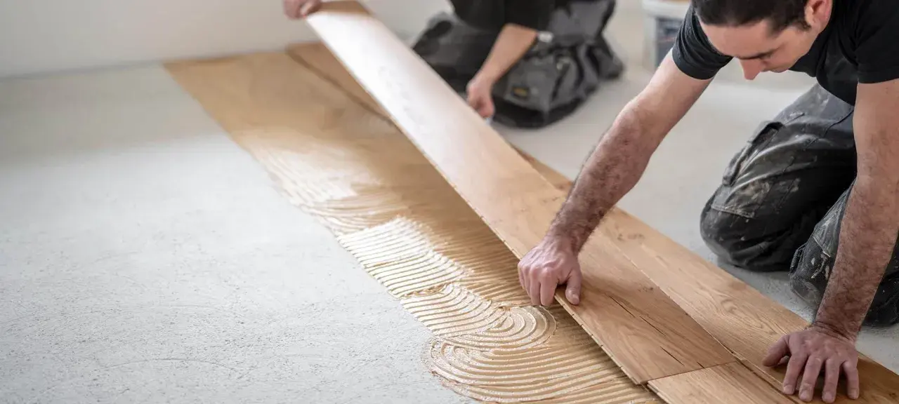 Handwerker verlegen sorgfältig Parkett auf Kleber. Die Holzbretter werden präzise nebeneinander gelegt, um ein schönes Ergebnis zu erzielen.