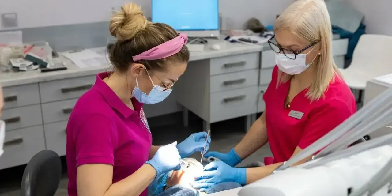 Dwie dentystki w różowych uniformach pracują przy pacjencie. Zastanawiasz się, po jakim czasie działa lekarstwo w zębie?