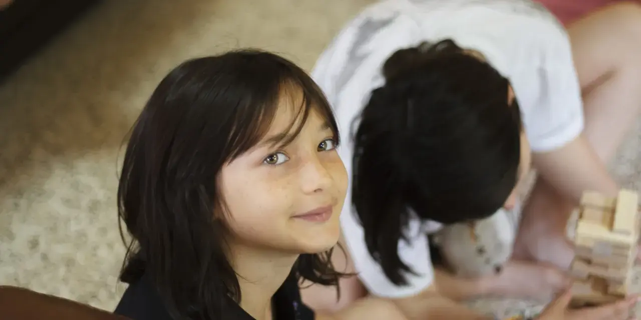 Deux enfants jouent à Jenga, une idée thème colonie. L'un regarde la caméra avec un sourire, l'autre est penché sur le jeu.