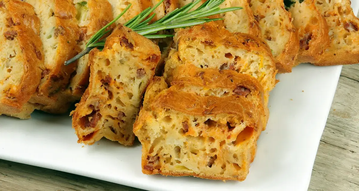 Tranches d'un cake salé au chorizo et poivron, garni de romarin, sur une assiette blanche.