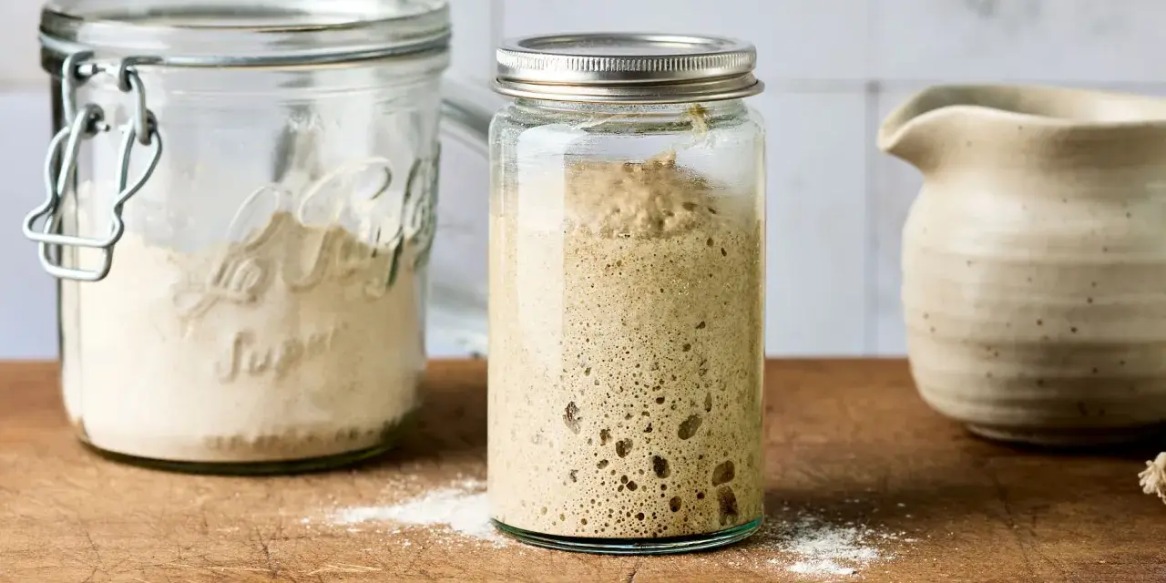 Blubbernder Sauerteig im Glas, bereit zum Backen. Daneben ein Glas mit Mehl, das zeigt, wie man den Sauerteig pflegen kann.