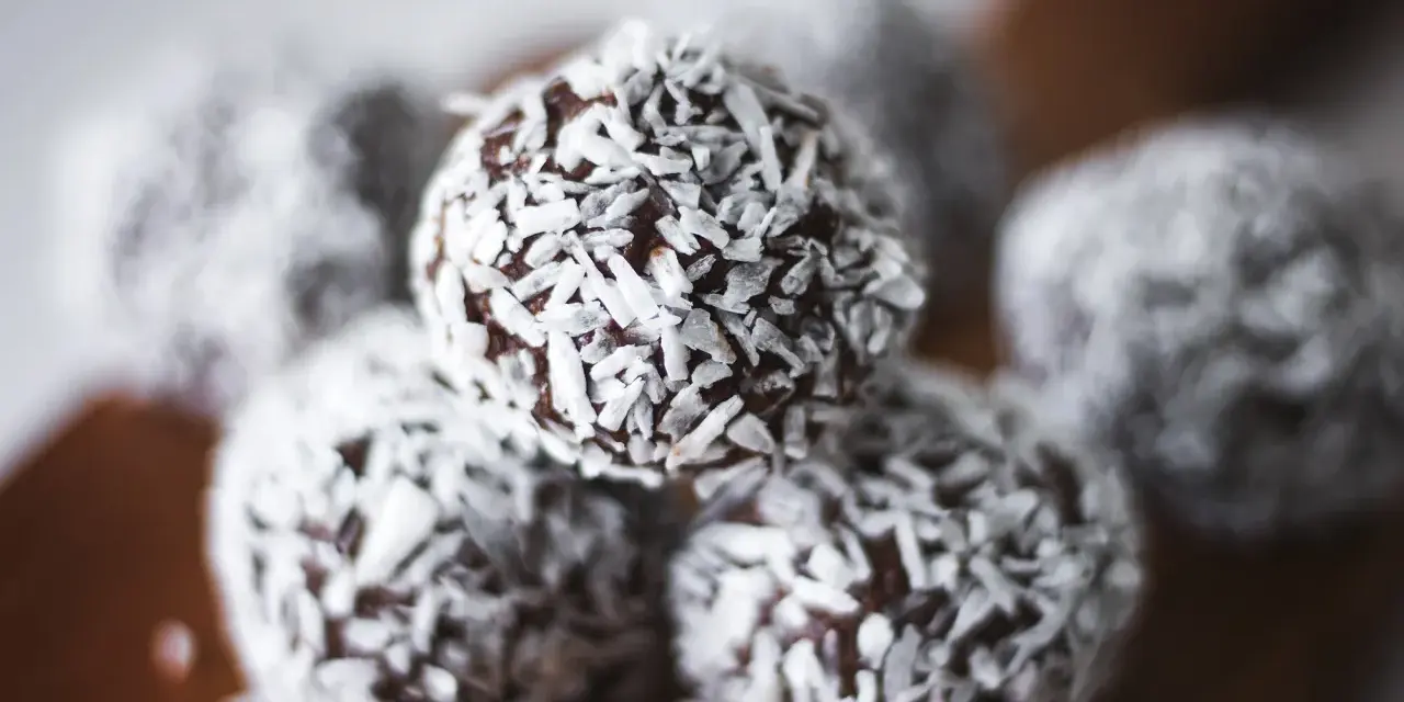Nära bild på protein chokladbollar täckta med kokosflingor. Perfekt för ett snabbt mellanmål.