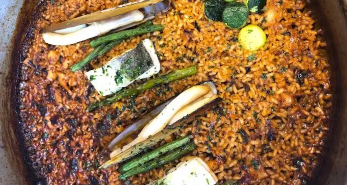 Deliciosa paella valenciana con arroz dorado, espárragos, pescado y navajas.
