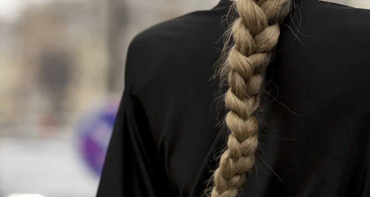Gruby, blond warkocz opada na czarne ramię. To jedna z tych fryzur z warkoczem, które przyciągają wzrok.
