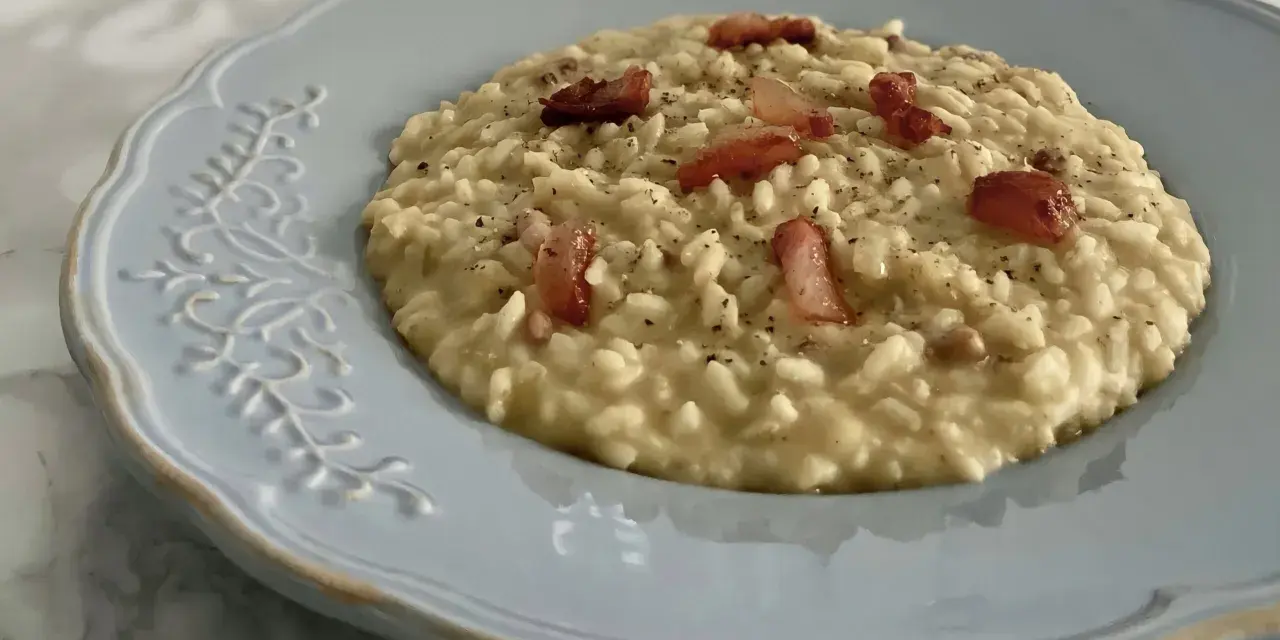 Un cremoso risotto con ceci e pancetta croccante, servito su un piatto azzurro decorato.