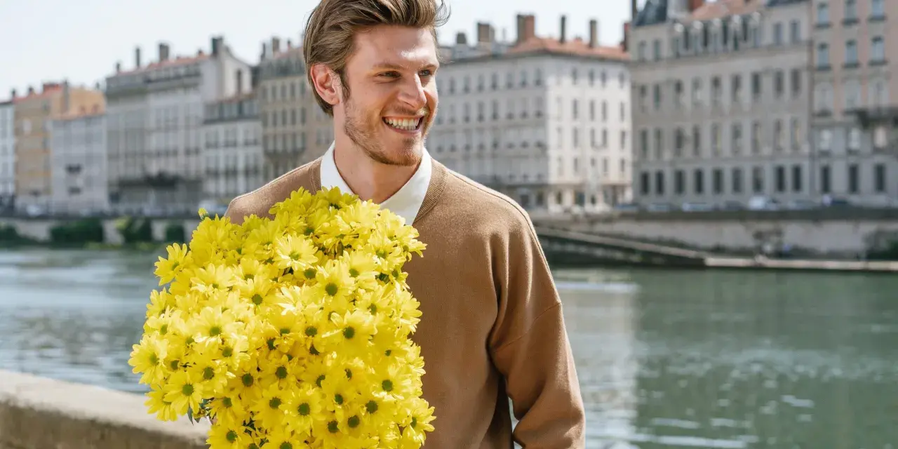 Hombre sonriente con un gran ramo de flores amarillas, quizás buscando el significado de flores para hombres.