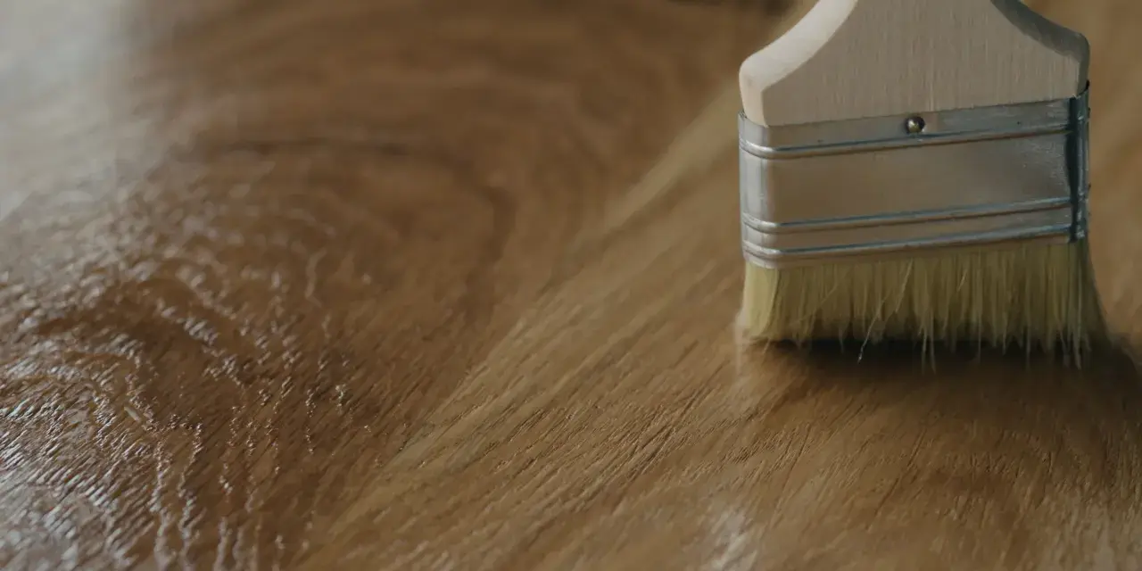 Brocha aplicando un acabado brillante sobre madera, mostrando diferentes tipos de barniz para madera.