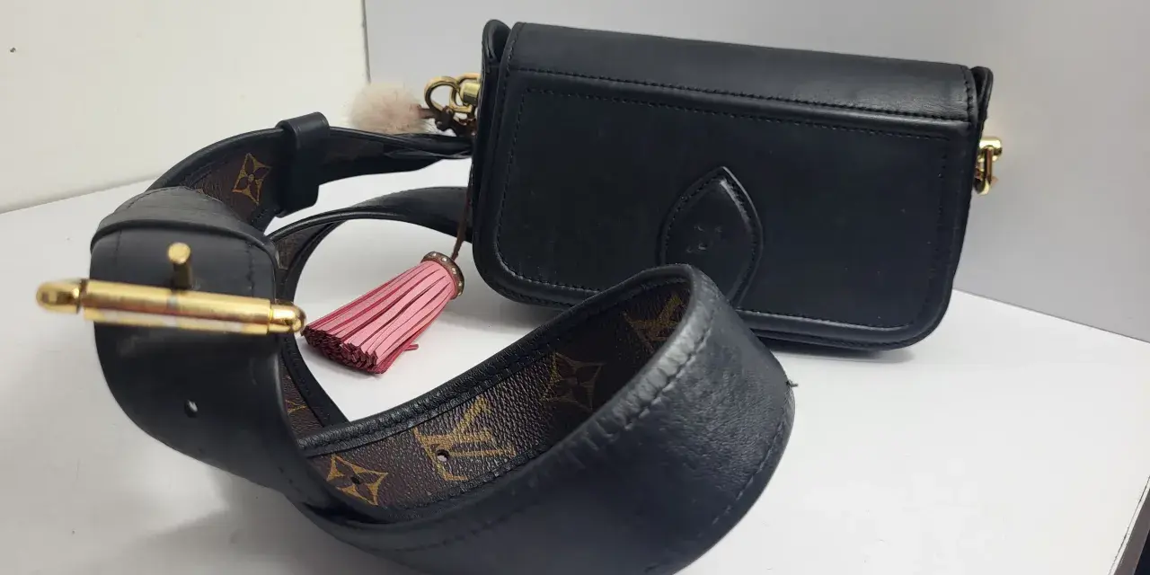 Elegancka, czarna louis vuitton torebka z ozdobnym, różowym pomponem i paskiem z monogramem.