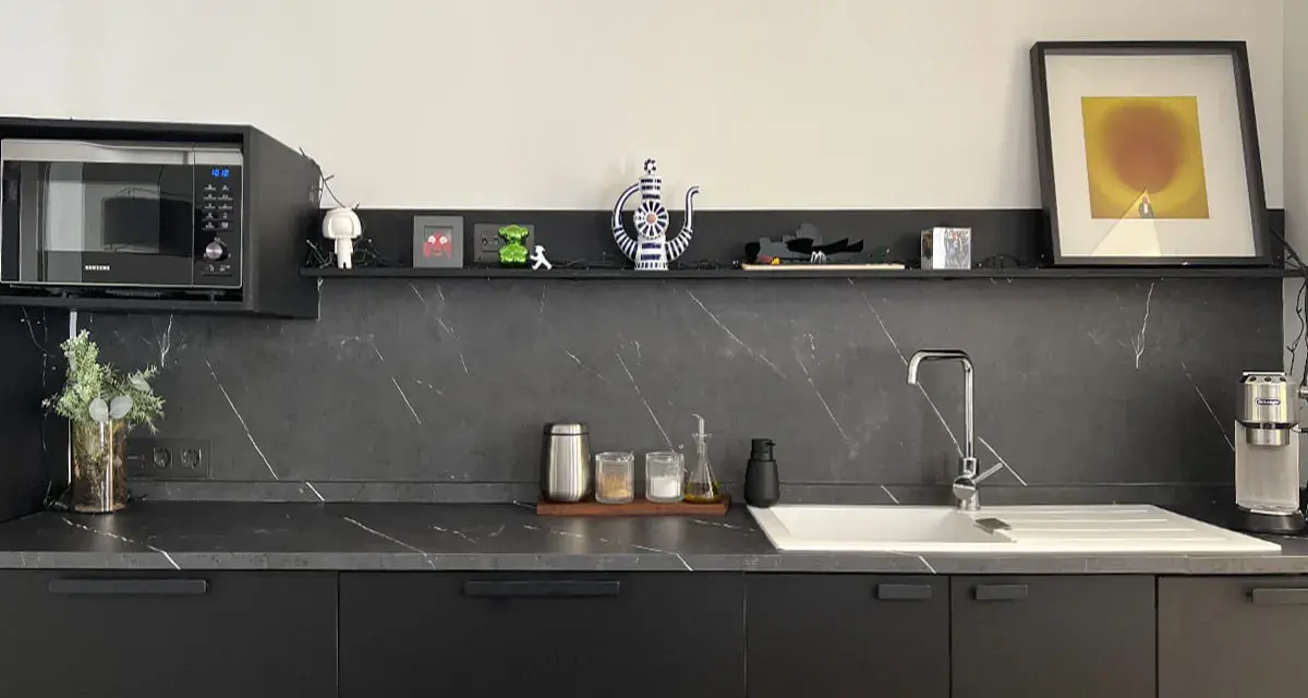 Encimera de cocina negra con vetas blancas, lista para cambiar. Microondas, fregadero y decoración moderna.