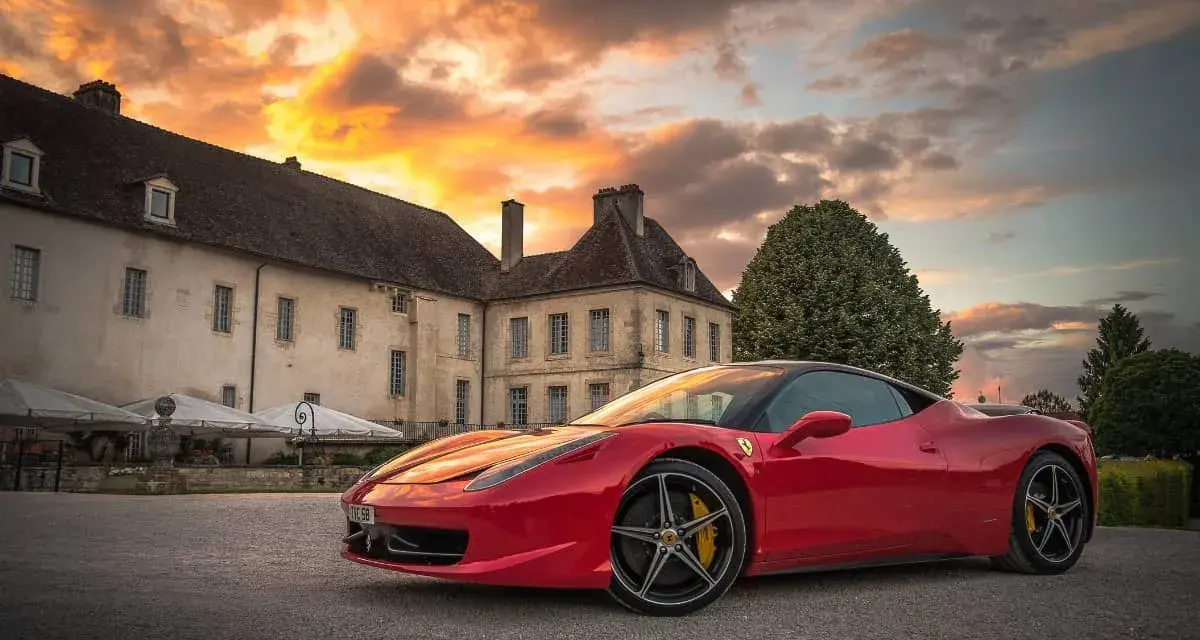 Czerwone Ferrari zaparkowane przed zabytkowym budynkiem podczas zachodu słońca.