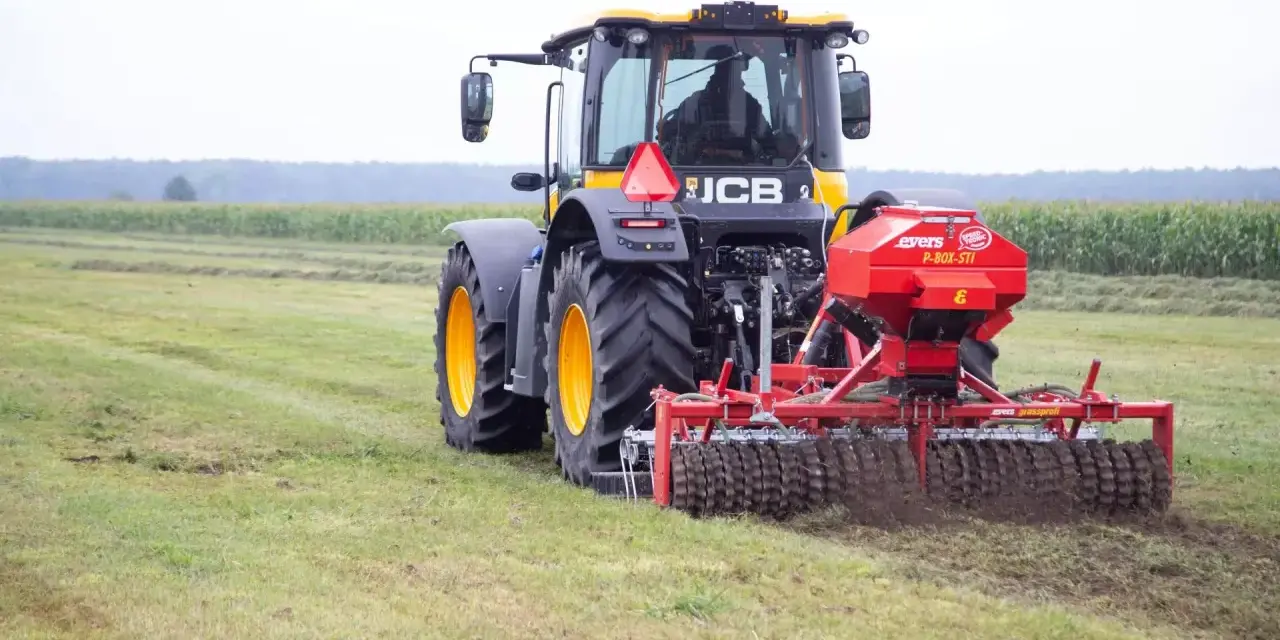 Ciągnik JCB z rozsiewaczem nawozu na polu.