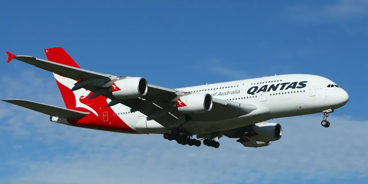 Gros avion Qantas, avec son logo rouge et blanc emblématique, en plein vol sous un ciel bleu.