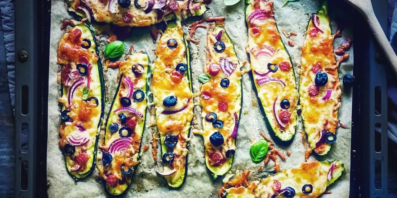 Zucchini-Hälften mit Käse, Oliven, Zwiebeln und Salami, die wie Pizza belegt sind. Sie schmeckt zucchini auf pizza!