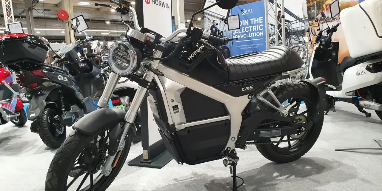 Czarny motocykl elektryczny Horwin CR6 na wystawie, obok innych skuterów.