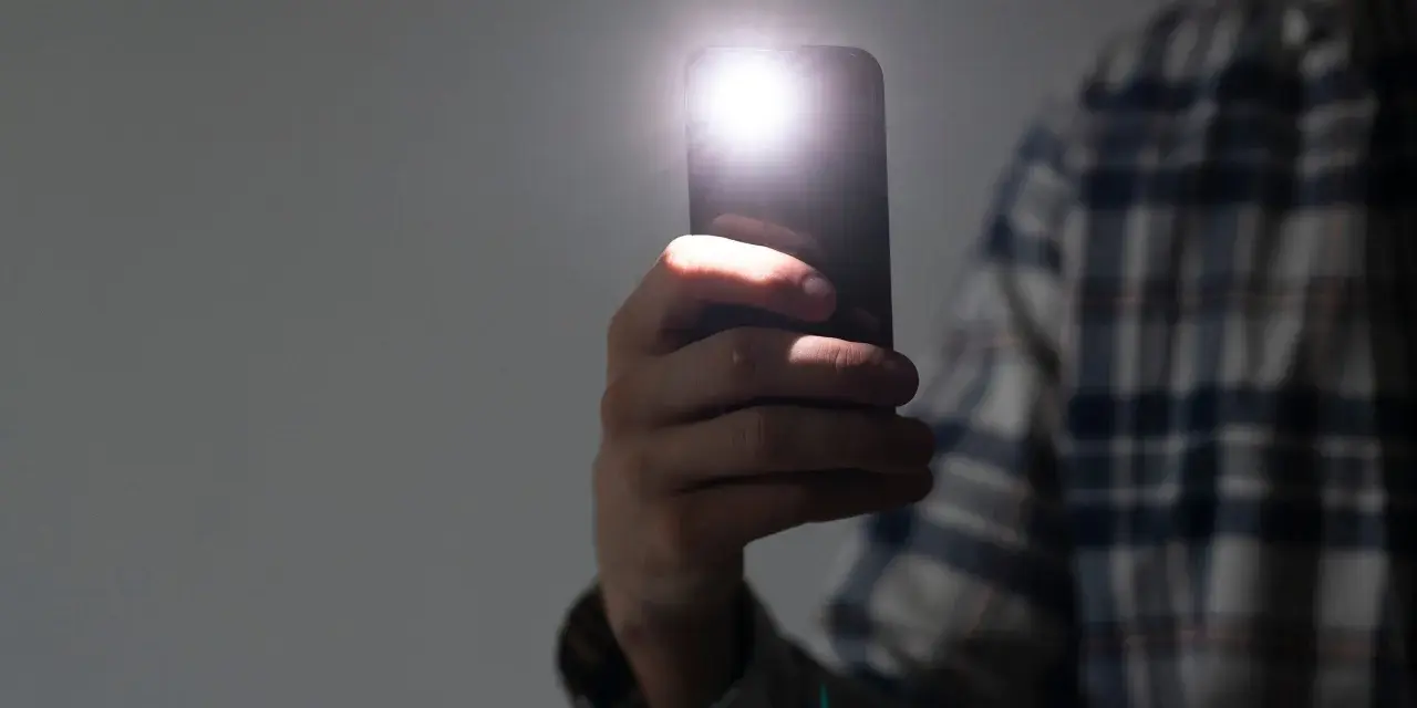 Dłoń trzyma smartfon z włączoną latarką.