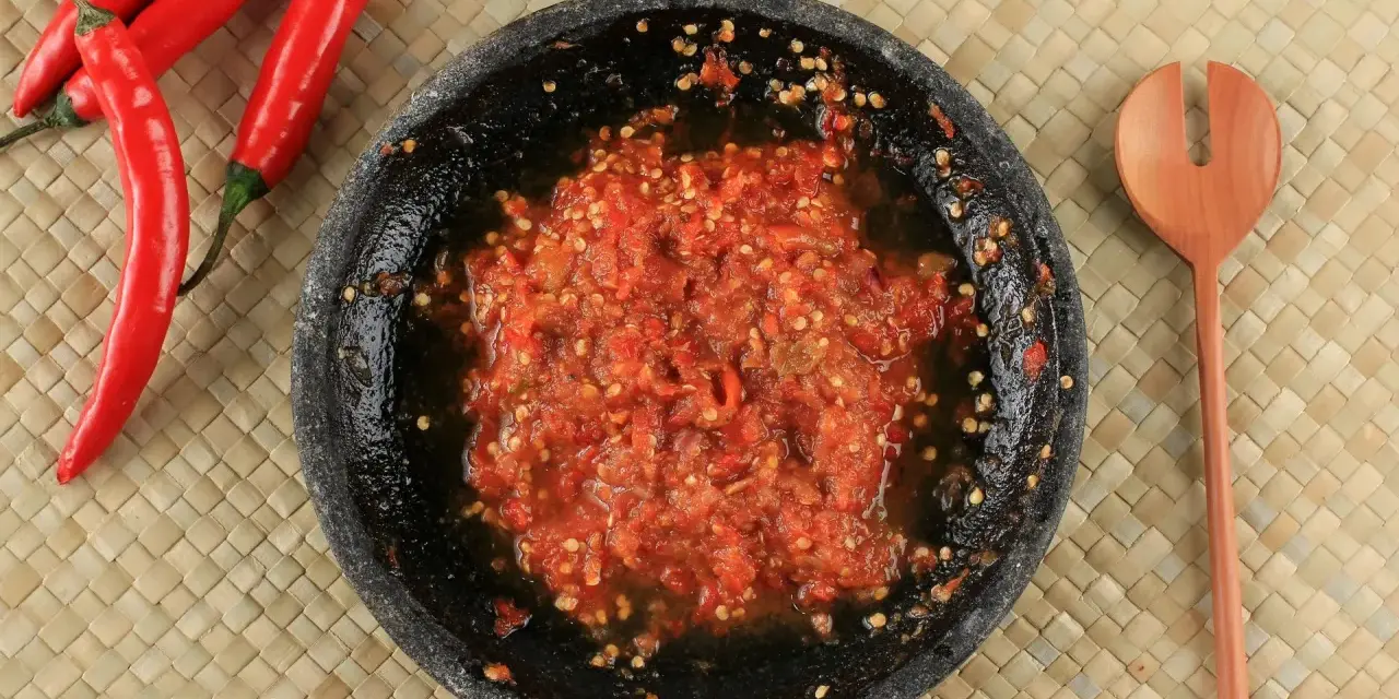 Świeżo przygotowany sos sambal w kamiennym moździerzu, obok czerwone papryczki chili i drewniana łyżka.