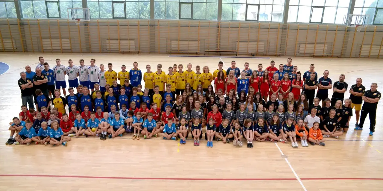 Drużyna Olimp Grodków na hali sportowej. Duża grupa dzieci i młodzieży w strojach sportowych pozuje do wspólnego zdjęcia.