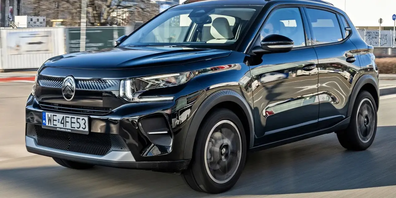 Czarny Citroen C3 porusza się po mieście, odbijając światła i budynki w swojej lśniącej karoserii.