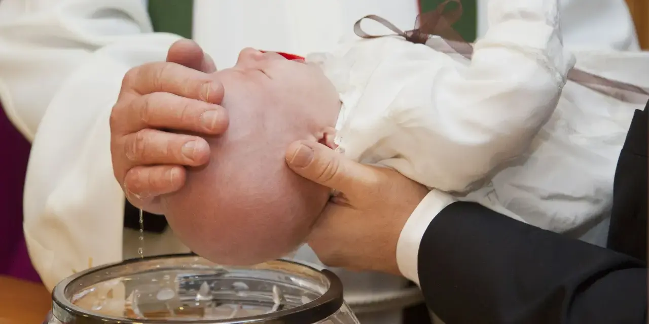 Chrzest chłopca: biała szatka, szklana chrzcielnica i woda święcona.