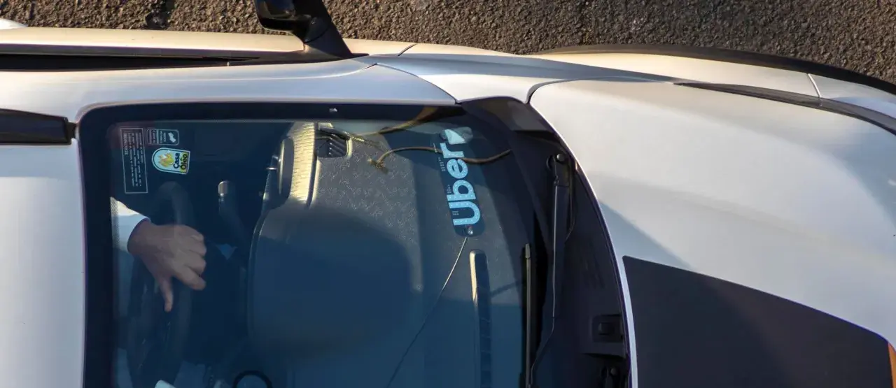 Fahrer hält das Lenkrad eines Autos mit Uber-Aufkleber auf der Windschutzscheibe.