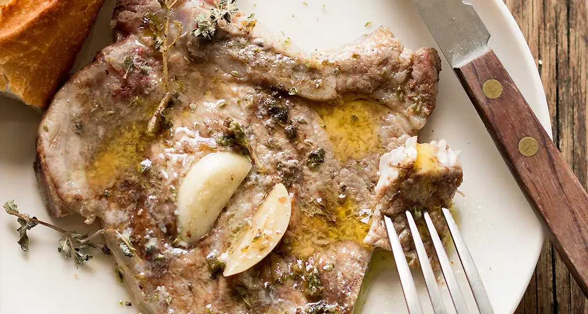 Succulenta braciola di maiale cotta con aglio e erbe aromatiche, servita con pane croccante.