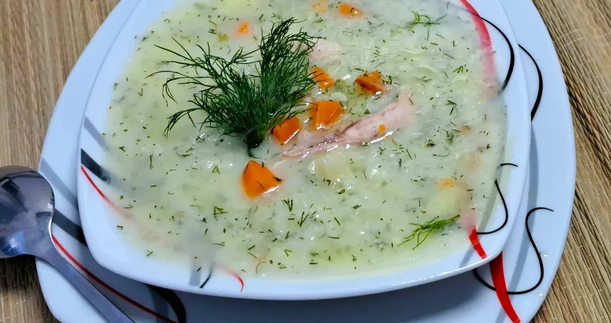Aromatyczna zupa koperkowa z ryżem, kawałkami kurczaka i marchewką, udekorowana gałązką koperku.