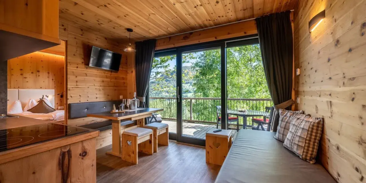 Przytulny domek z widokiem na góry, idealny na camping Seiser Alm. Drewniane wnętrze, wygodna kanapa i stół zapraszają do relaksu.