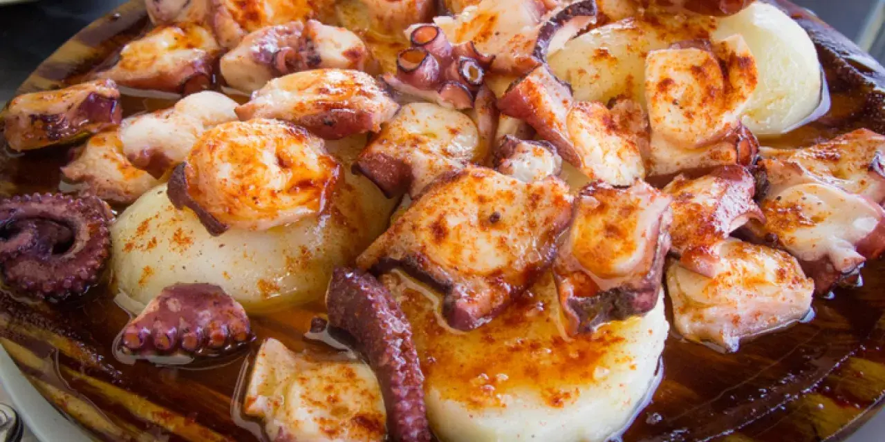 Pulpo a la gallega servido en plato de madera, con patatas cocidas y espolvoreado con pimentón.