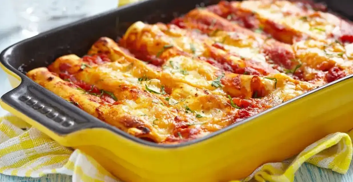 Pyszne cannelloni z mięsem mielonym, zapieczone pod sosem pomidorowym i serem, w żółtym naczyniu.