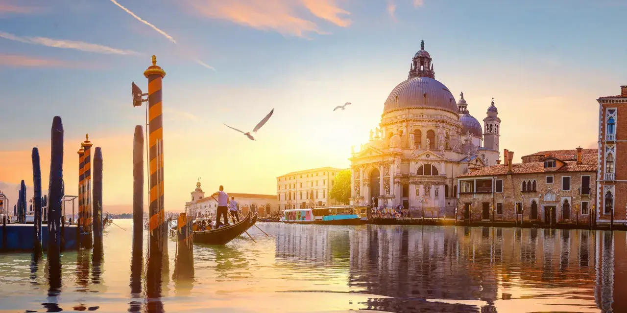 Gondola che scivola sull'acqua al tramonto, con la Basilica di Santa Maria della Salute sullo sfondo. Un'indimenticabile attività a Venezia.