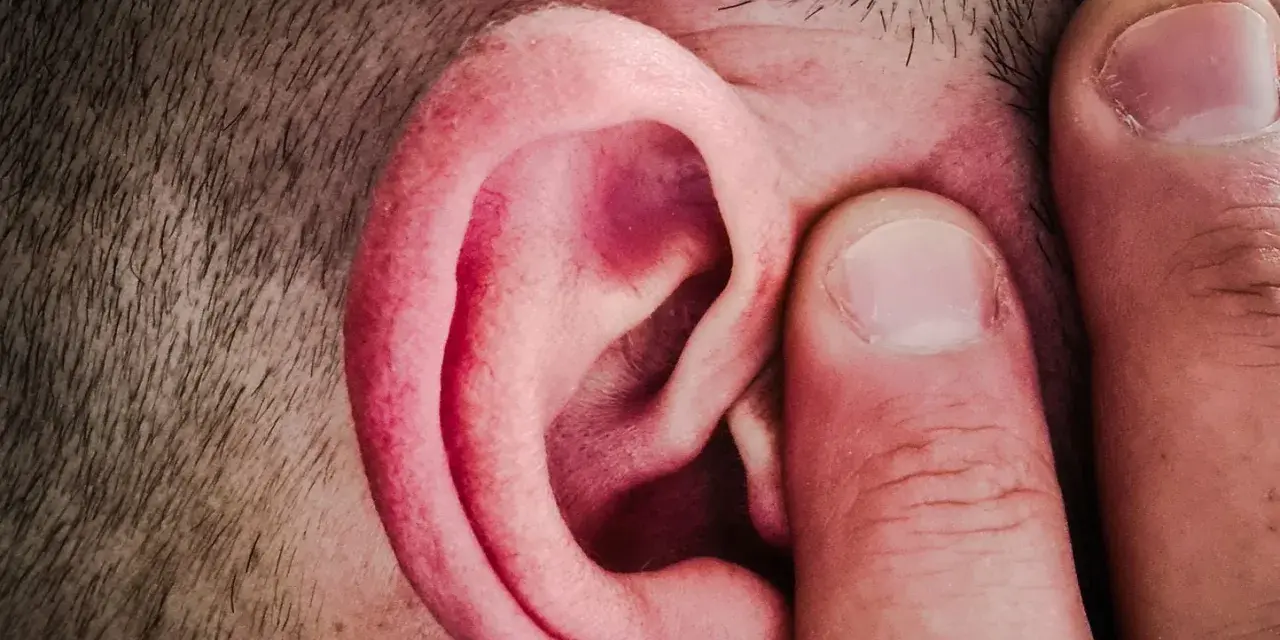Un doigt pince l'oreille d'un homme, comme pour mieux capter un son aigu.