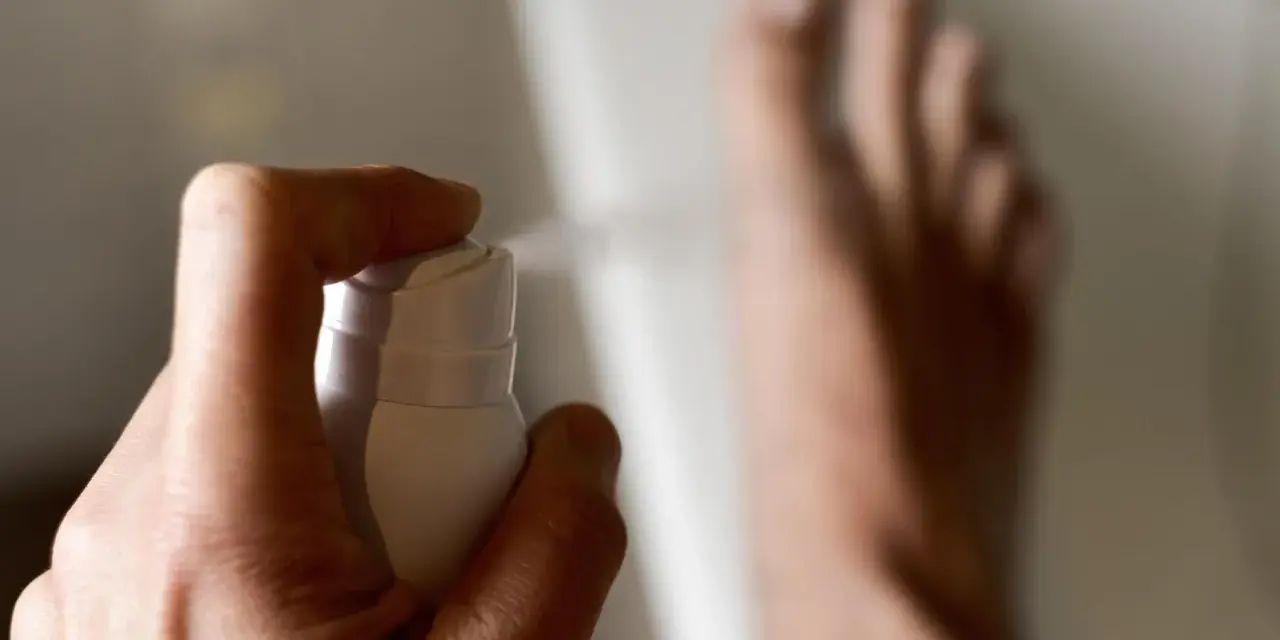 Main tenant une bombe, vaporisant un produit sur son pied pour lutter contre la transpiration.