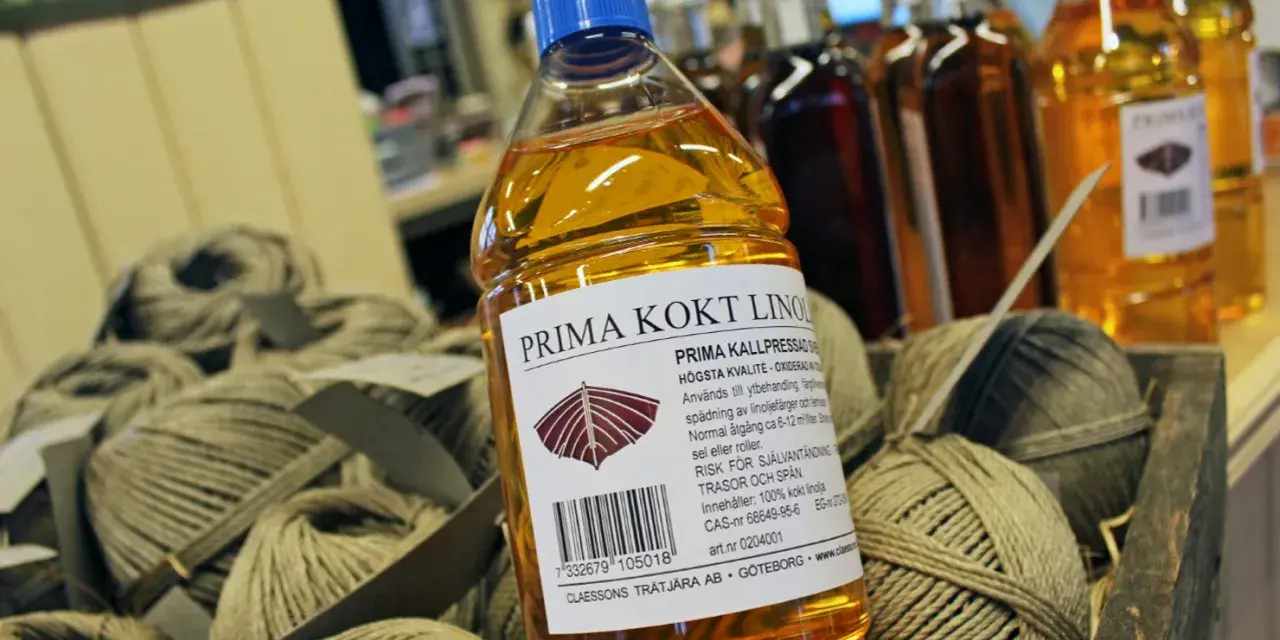 En flaska Prima kokt linolja, perfekt för fernissa oljemålning och ytbehandling av trä. Bredvid ligger härvor av garn.