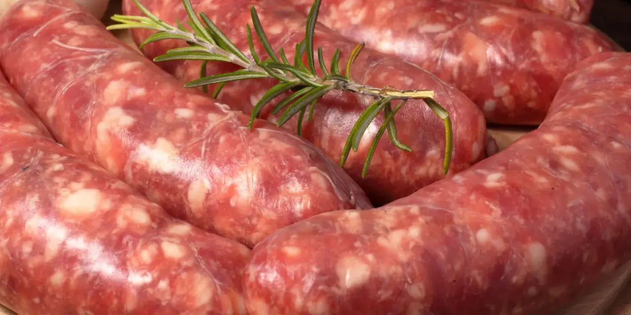 Salsiccia co to? Surowe kiełbaski wieprzowe, przyprawione ziołami, leżą na desce.