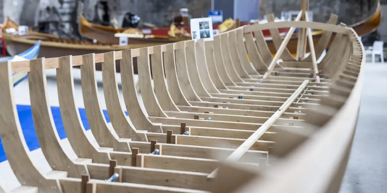 Struttura in legno di una barca veneziana in costruzione, con altre imbarcazioni sullo sfondo.