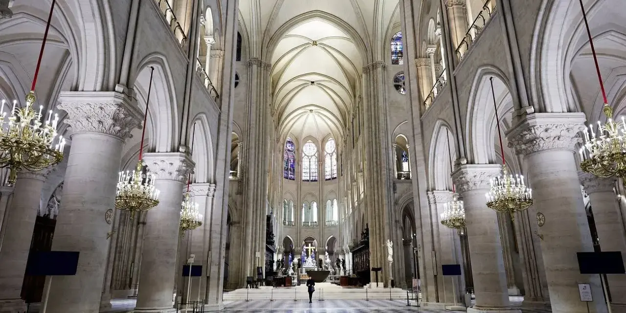 Wnętrze katedry Notre Dame, z monumentalnymi kolumnami, sklepieniem i witrażami. Na środku nawy stoi samotna postać.