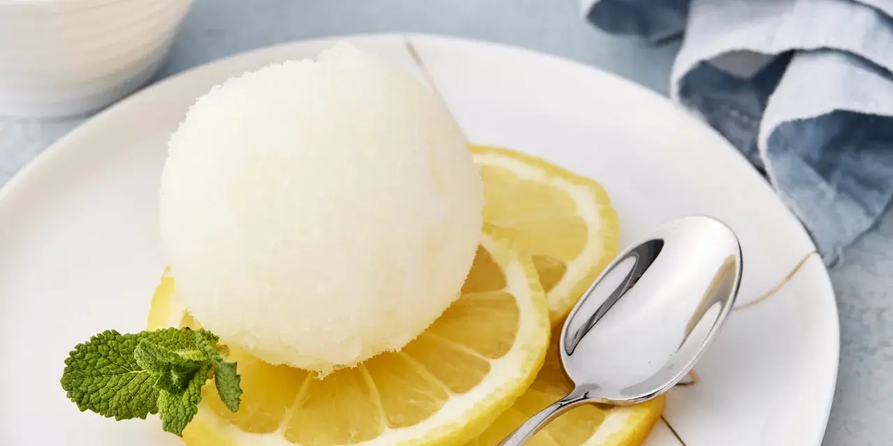 Erfrischendes Zitronensorbetto-Rezept: Eine Kugel Sorbet auf Zitronenscheiben mit Minze und Löffel.