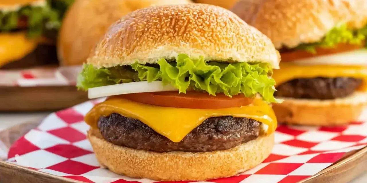 Soczysty burger z serem, sałatą, pomidorem i cebulą na czerwono-białej kratce.