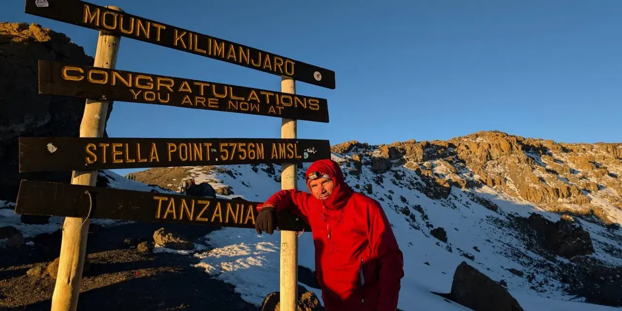Mężczyzna w czerwonej kurtce przy znaku "Mount Kilimanjaro, Stella Point". To właśnie tutaj jest Kilimandżaro!